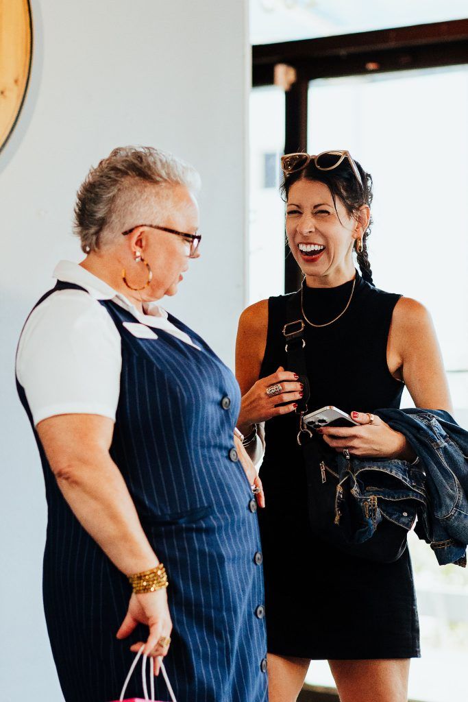 female business owners talking and laughing with each other in front of natural lighting through windows