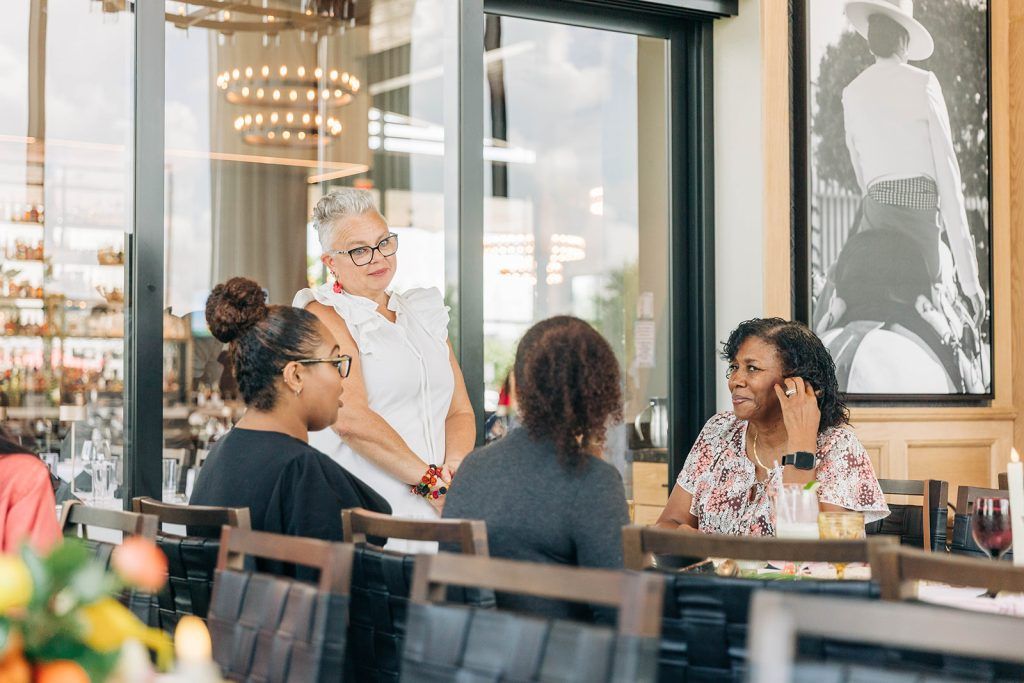 Group of women business owners speaking at a networking event with the networking host standing at the end of the table listening.
